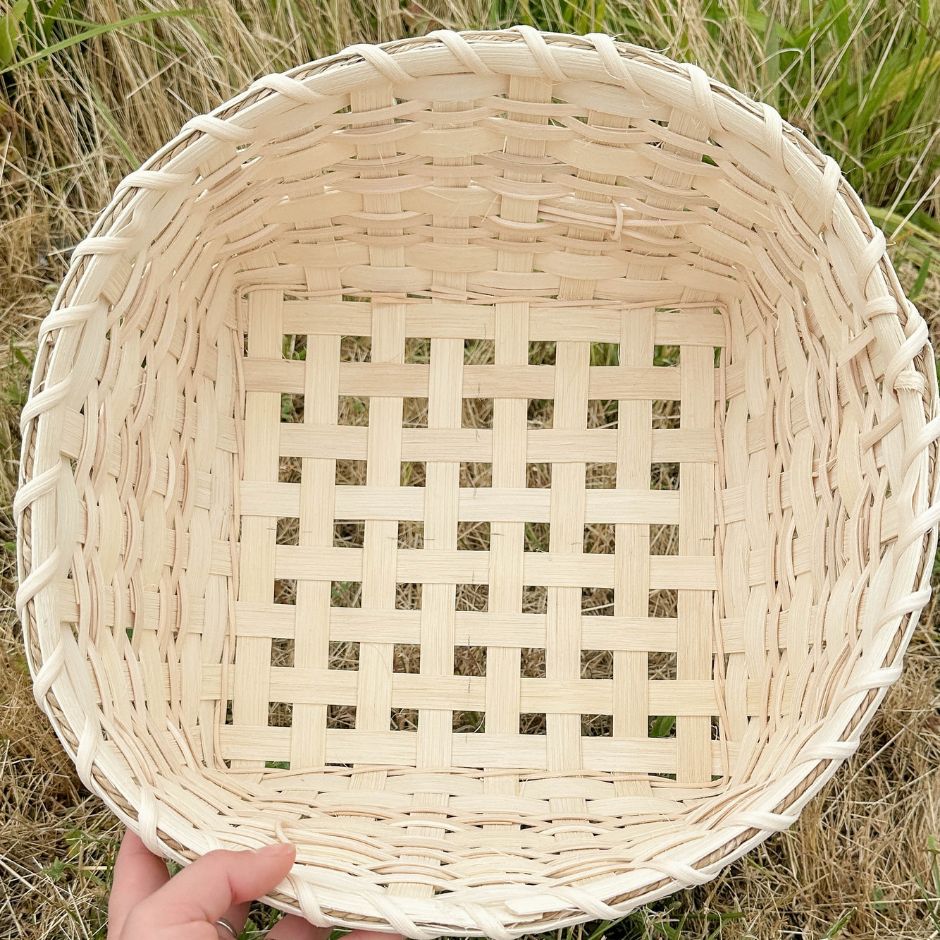 Top inside view of a cross-stitch napkin basket sitting in the grass. Image shoes off the open weave technique in the base of the basket.