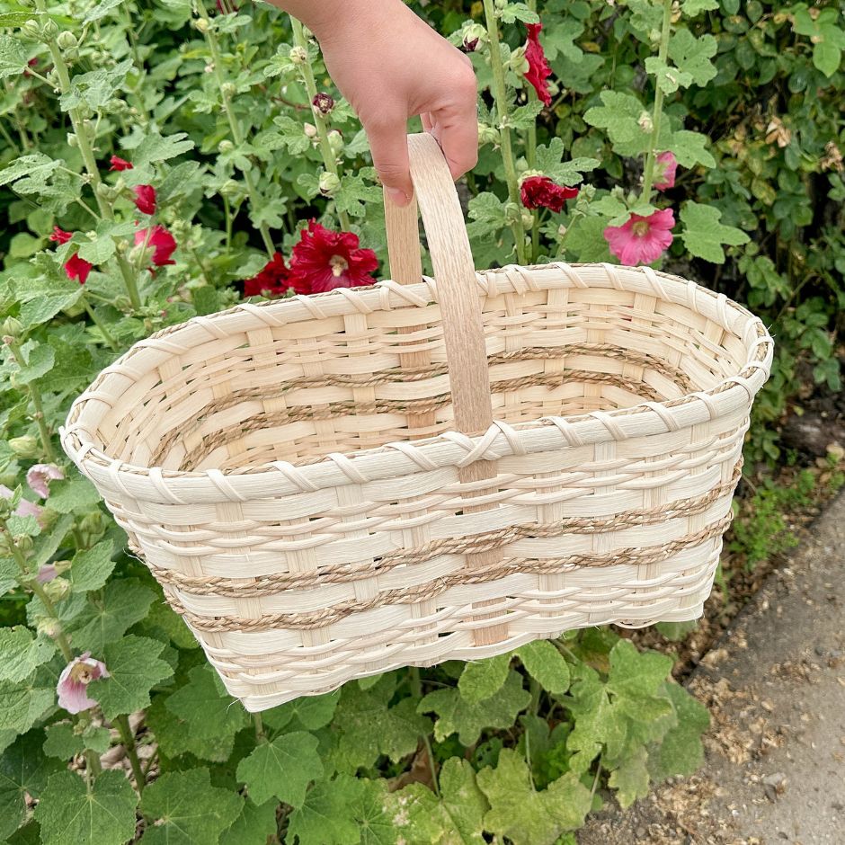 Woman's hand holding a market basket against a backdrop of hollyhocks.
