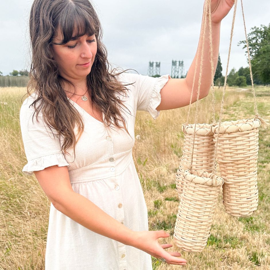 Woman in a white linen dress holding a trio of hanging vase baskets.
