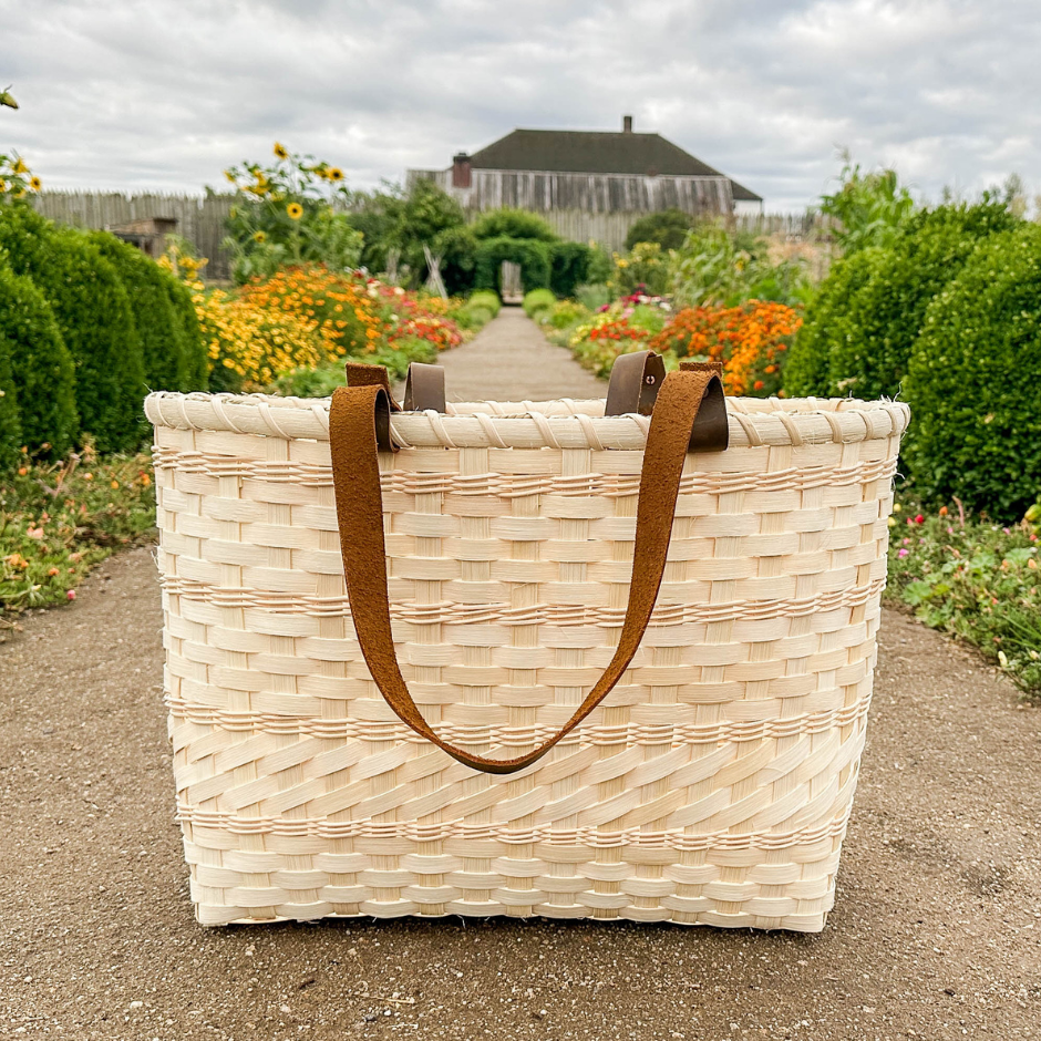 Woven basket with brown leather handles on a garden path