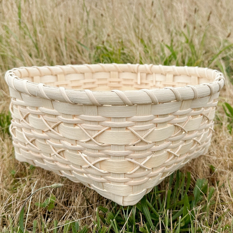 Cross-stitch napkin basket sitting in the grass.
