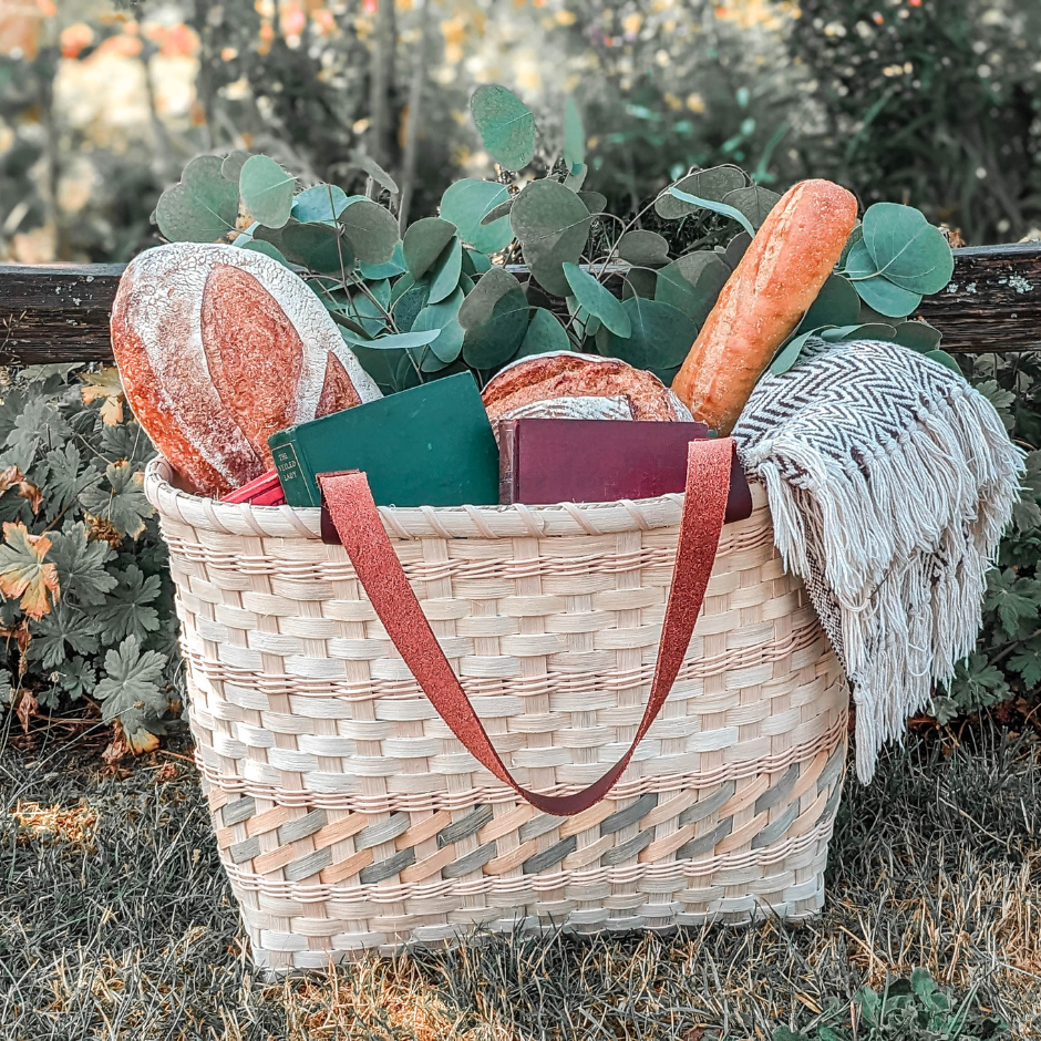 Woven basket with picnic items including bread and books, set against a natural background.