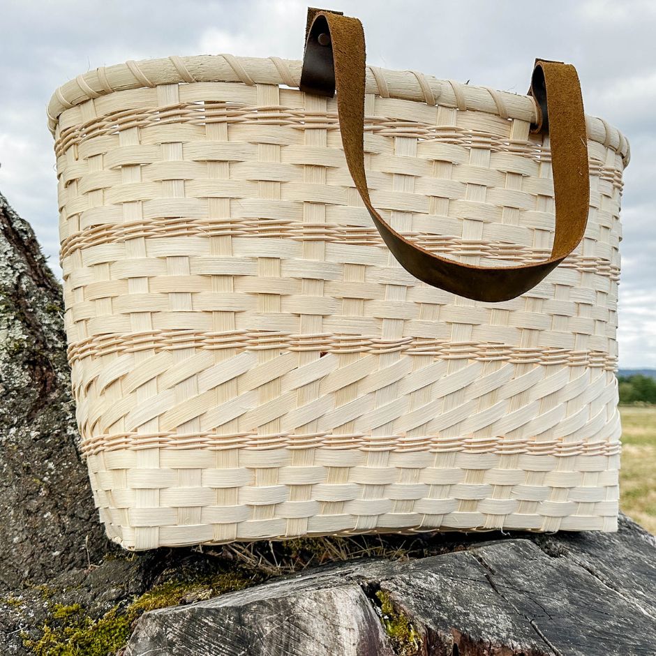 Woven basket with brown leather handles sitting on a tree stump.