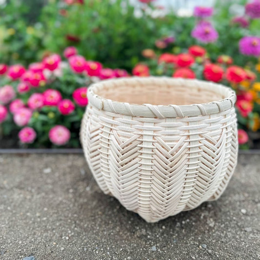Catshead basket with detailed chevrons sits against a flower garden.