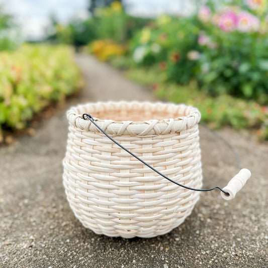 A bean pot basket sitting on a garden path. Blurred flower beds line either side of the path.
