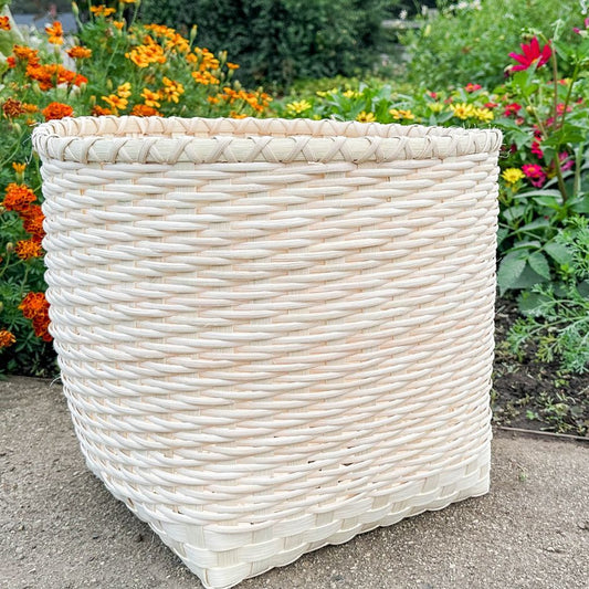 Twill Basket Blanket sits on the garden path with a flower garden in the background.