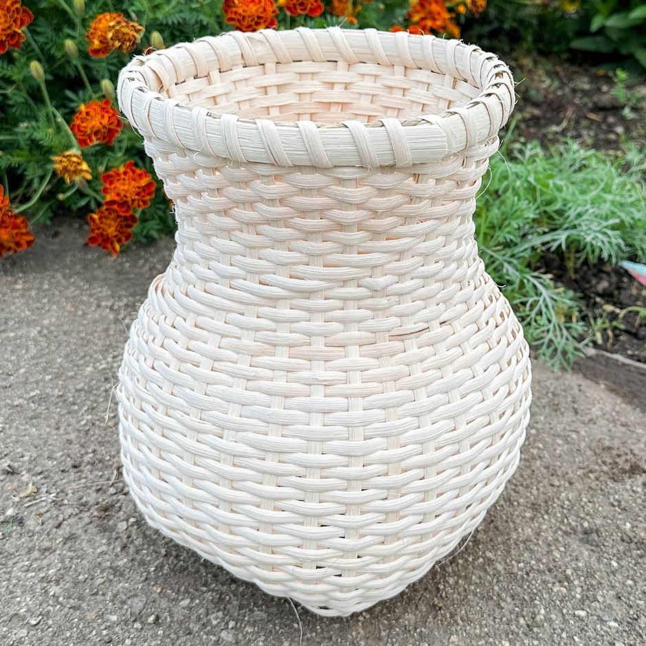 Load video: Rattan stair step vase basket sitting in a garden of marigolds.