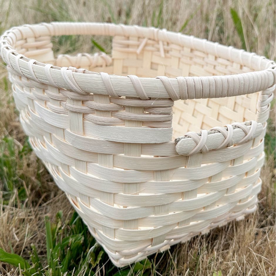 A woven reed basket with built in handles sits in the grass.