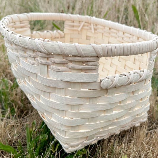 A woven reed basket with built in handles sits in the grass.