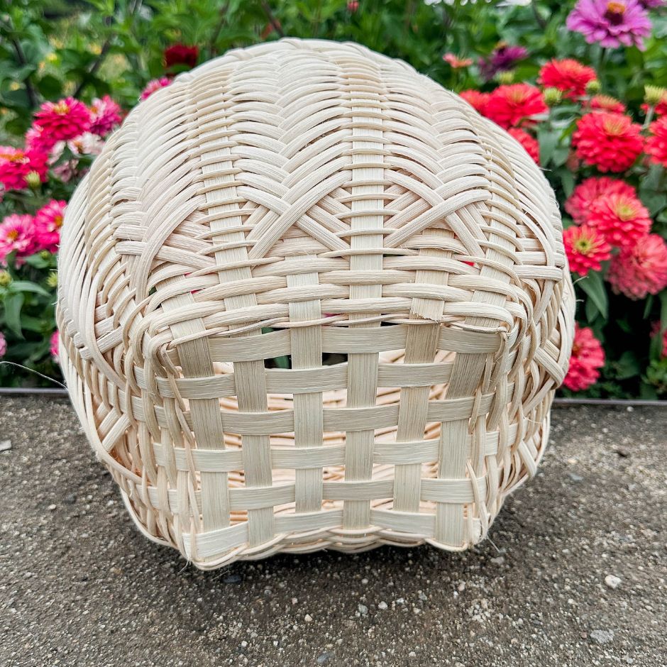 Catshead basket with detailed view of the bottom sits against a flower garden.