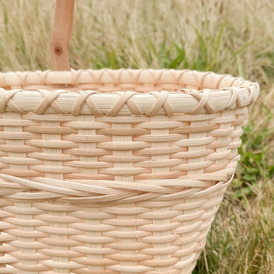 Detail of the market basket braiding technique and the rim. Basket is sitting against a grassy backdrop. 
