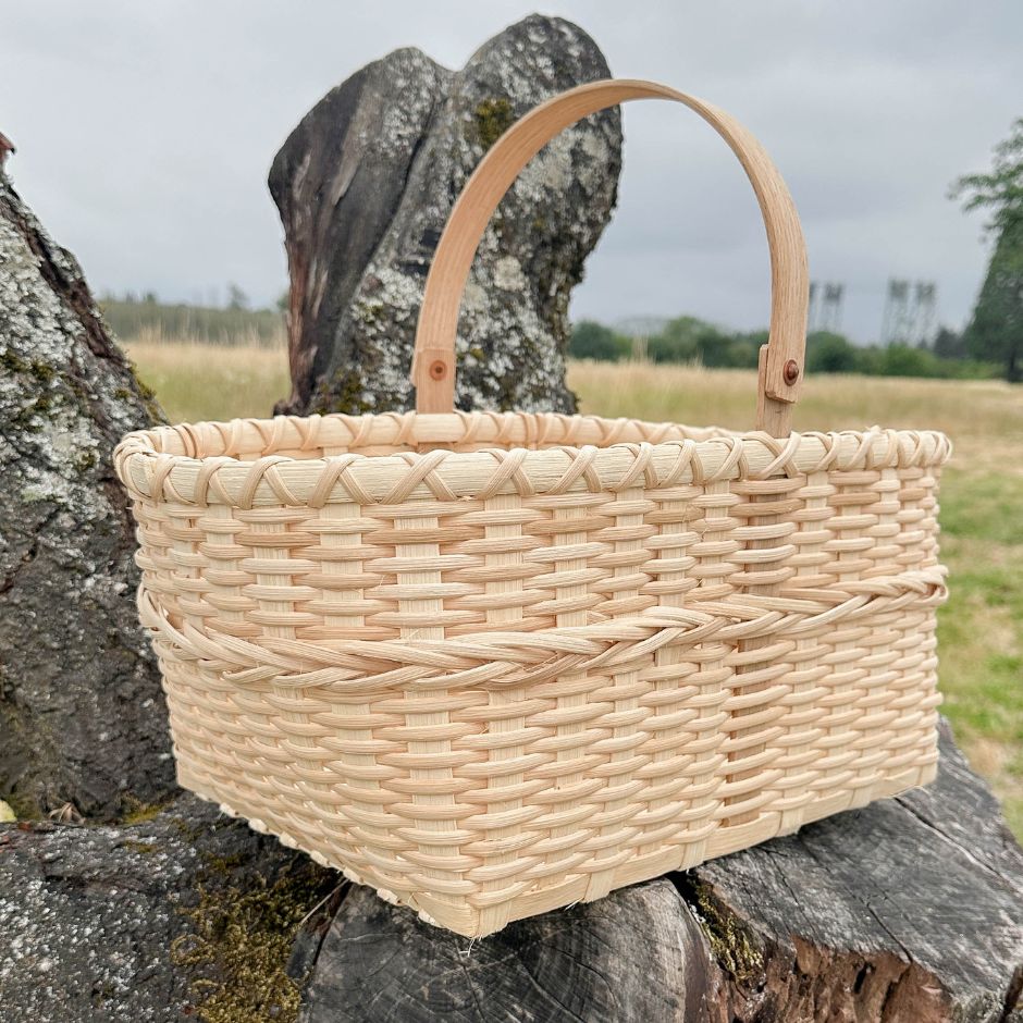 A woven rattan reed basket with handle on a wood stump surface in a natural setting