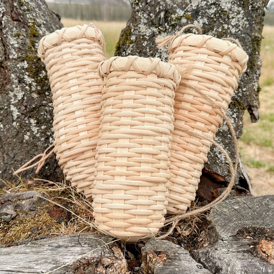 A trio of hanging vase baskets is propped up against a lichen covered tree trunk. 