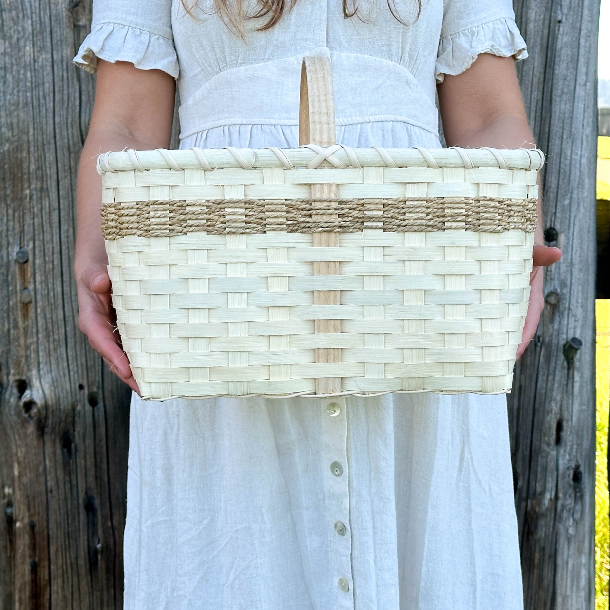 Person holding a woven basket against a wooden fence background