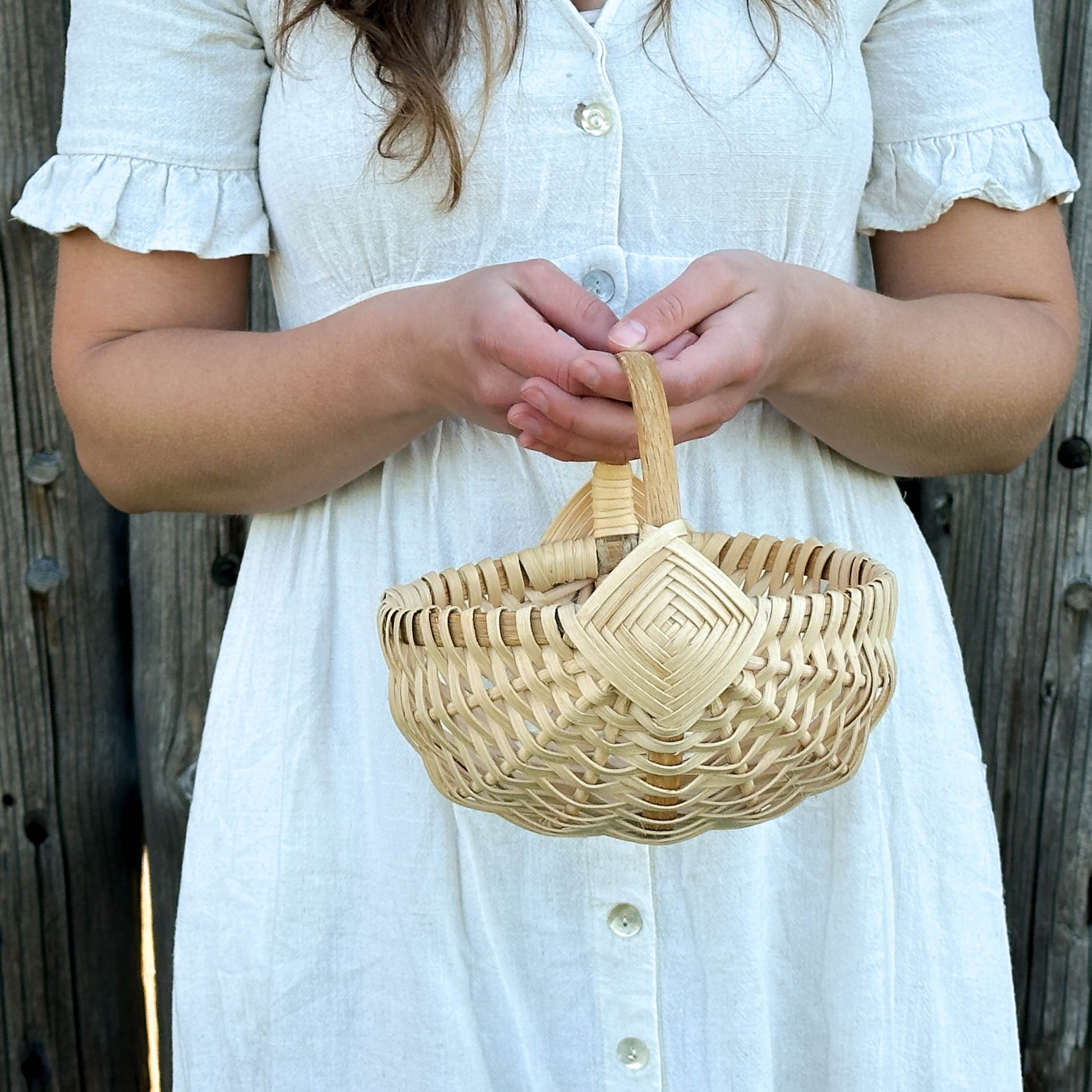 Person holding a woven basket against a wooden fence background