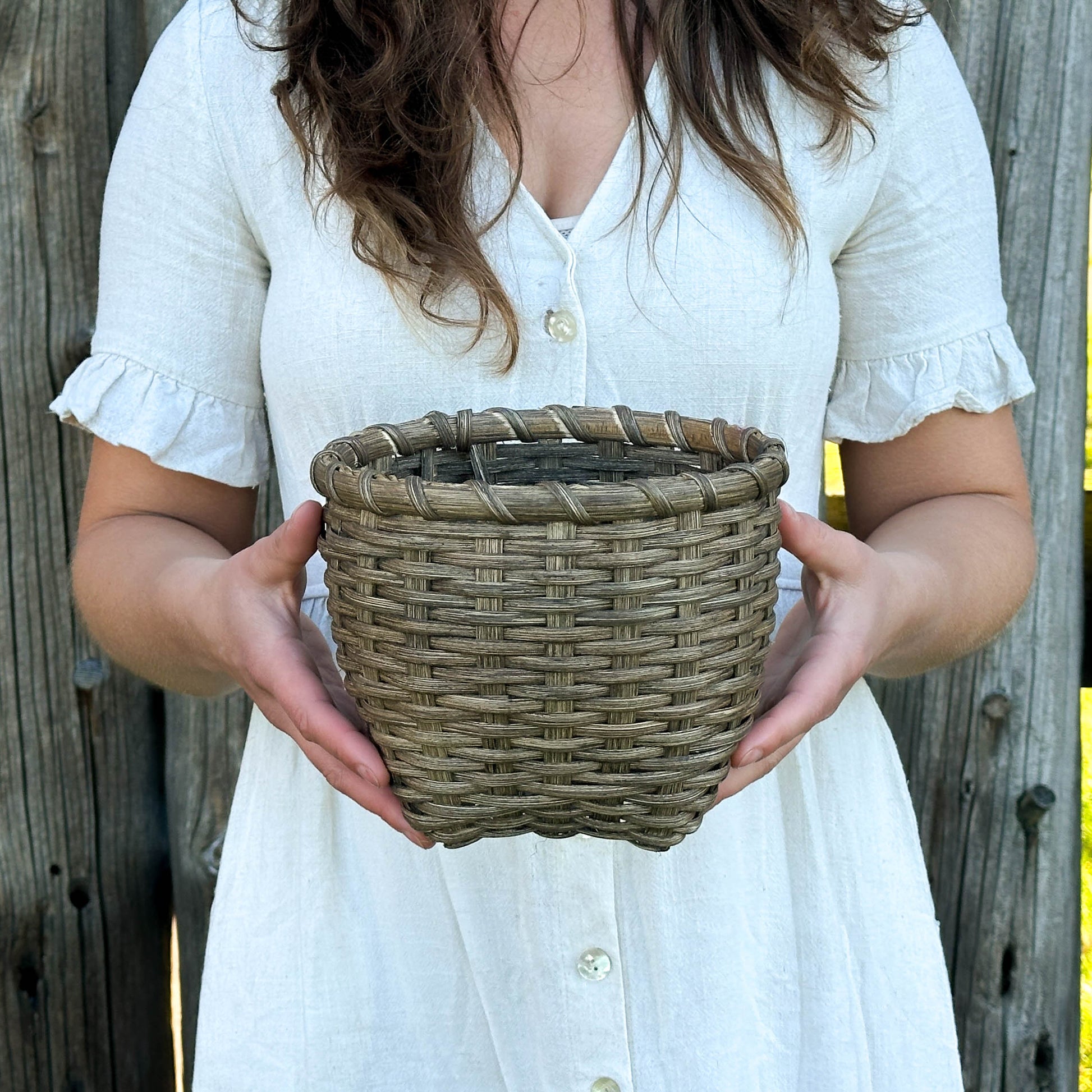 Woman holding a woven basket in front of a wooden fence