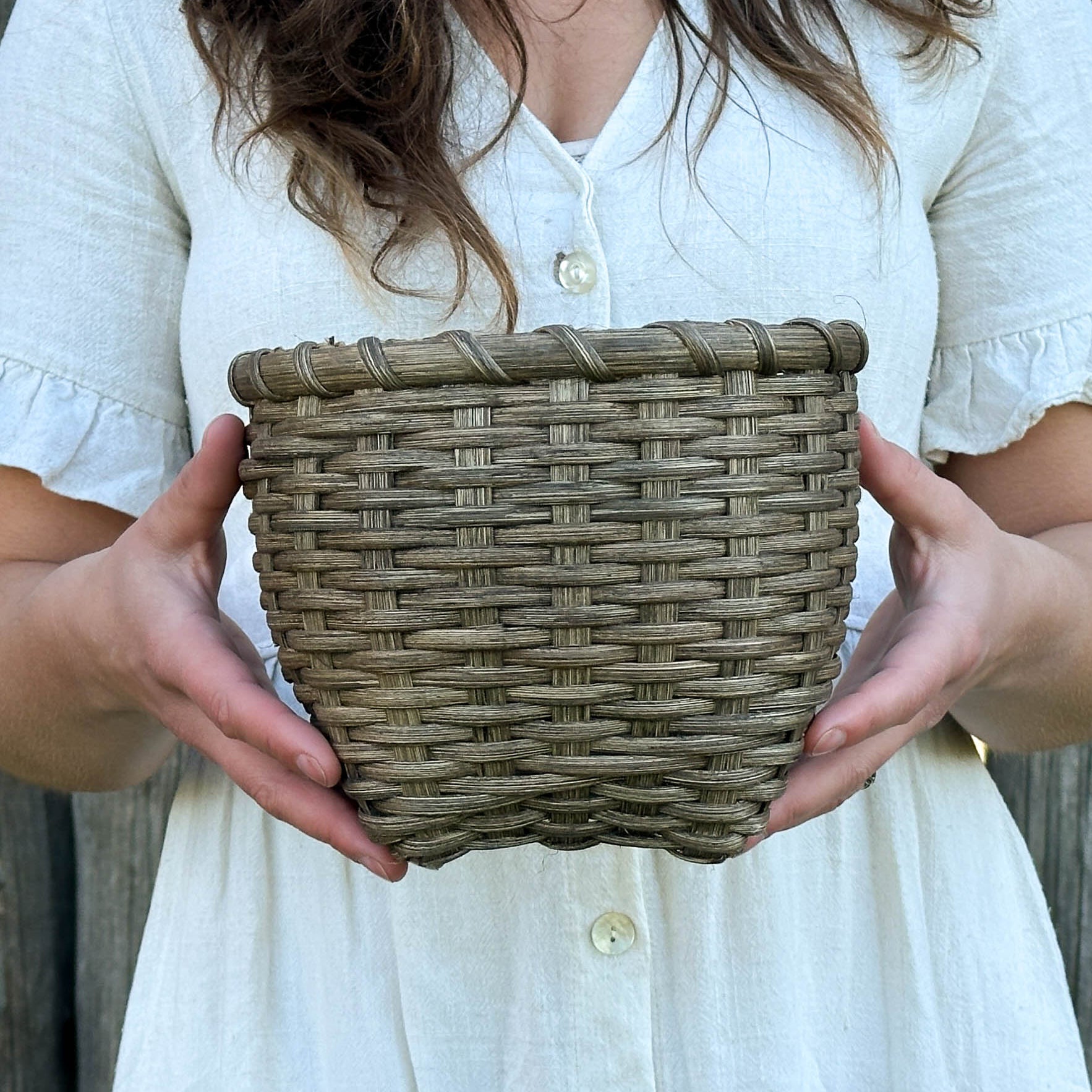 Woman holding a woven basket in front of a wooden fence