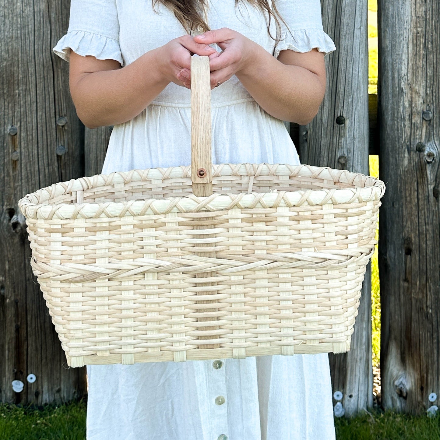 Woman holding a woven basket against a wooden fence.