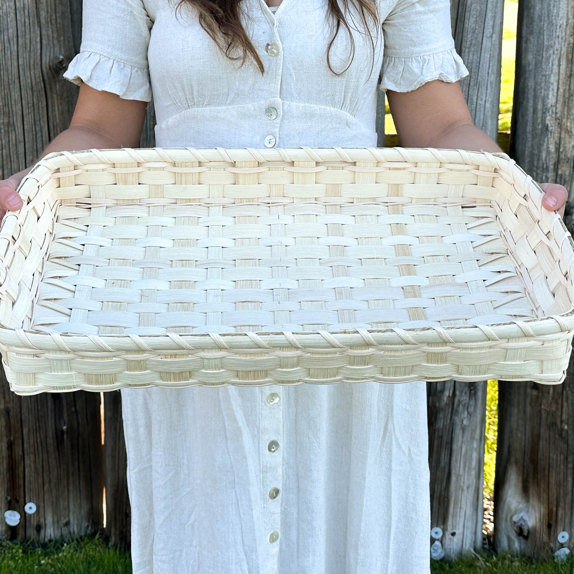 Person holding a woven tray in front of a wooden fence