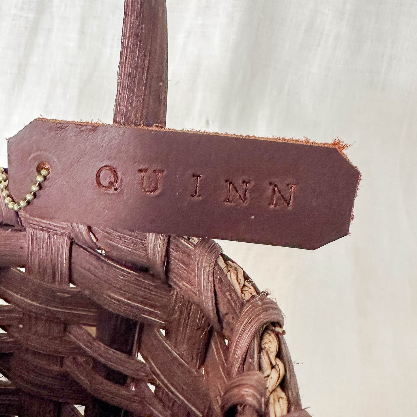 Brown woven basket with a leather tag labeled 'QUINN' on a white background