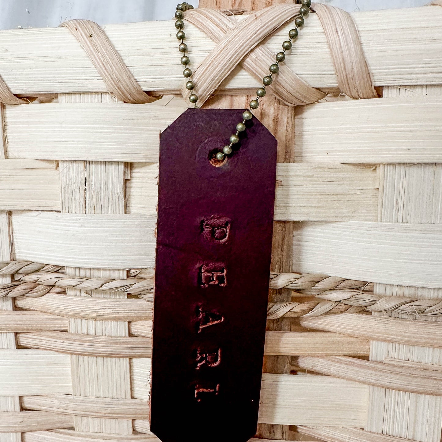 Brown leather tag with 'PEARL' engraved on it, attached to a woven basket.