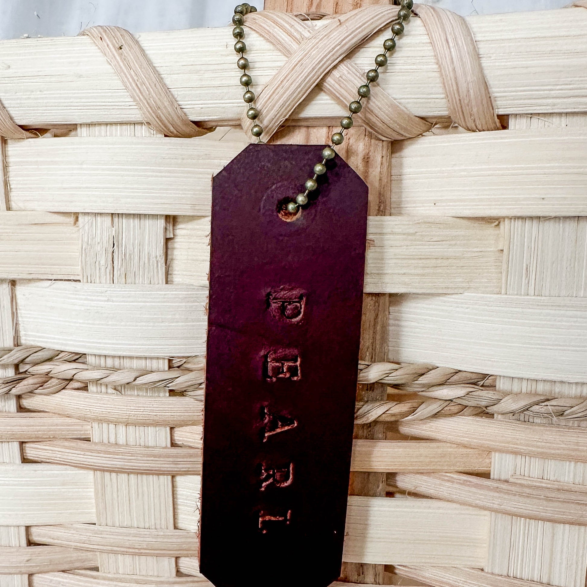 Brown leather tag with 'PEARL' engraved on it, attached to a woven basket.