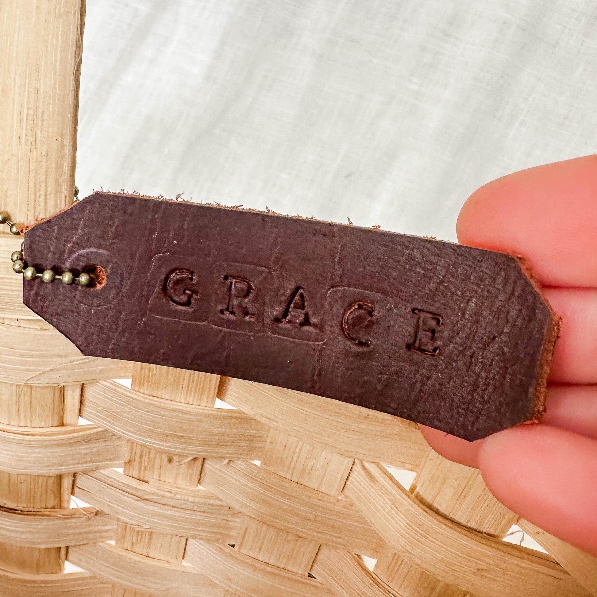 Brown leather tag with 'GRACE' engraved on it held over a woven basket.