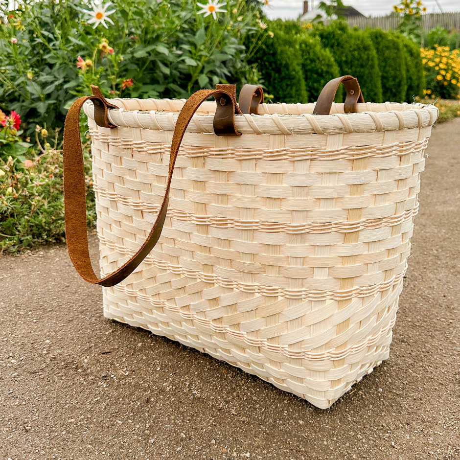 Woven basket with leather handles on a garden path.