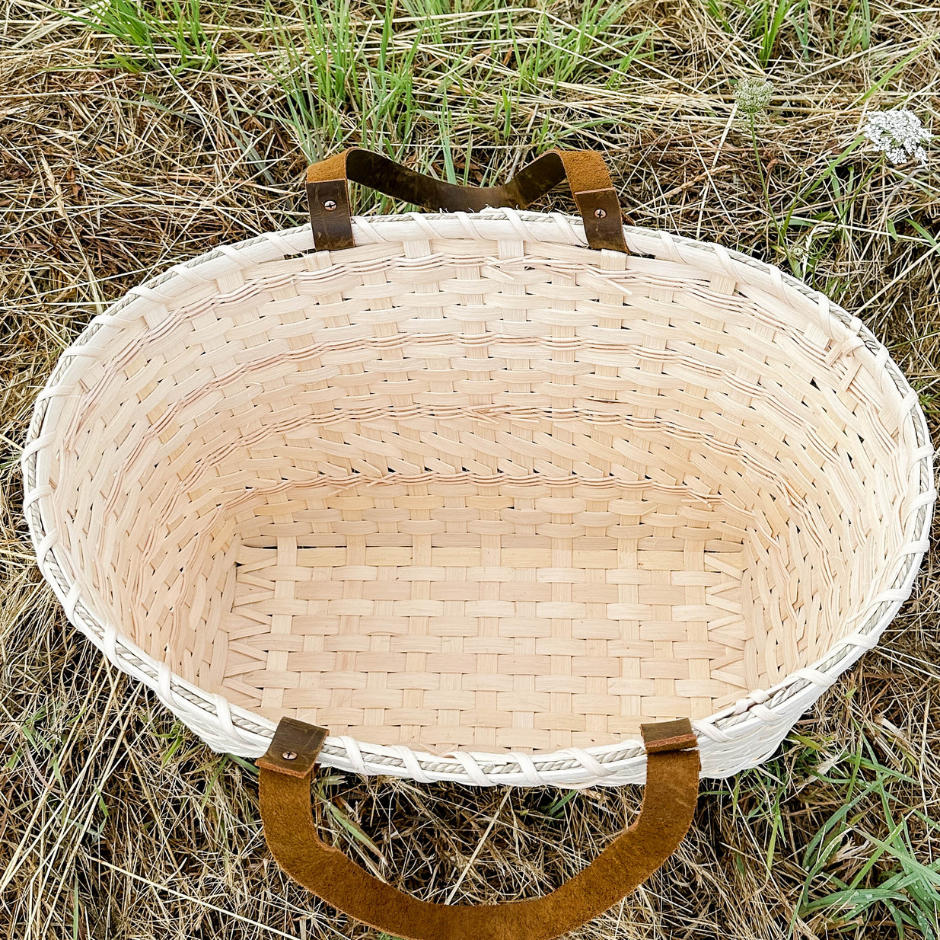 Woven basket with brown handles on a grassy background.